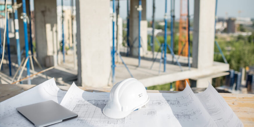 Workspace at the construction site Workspace with architectural drawings laptop and protective helmet at the table on the construction site
